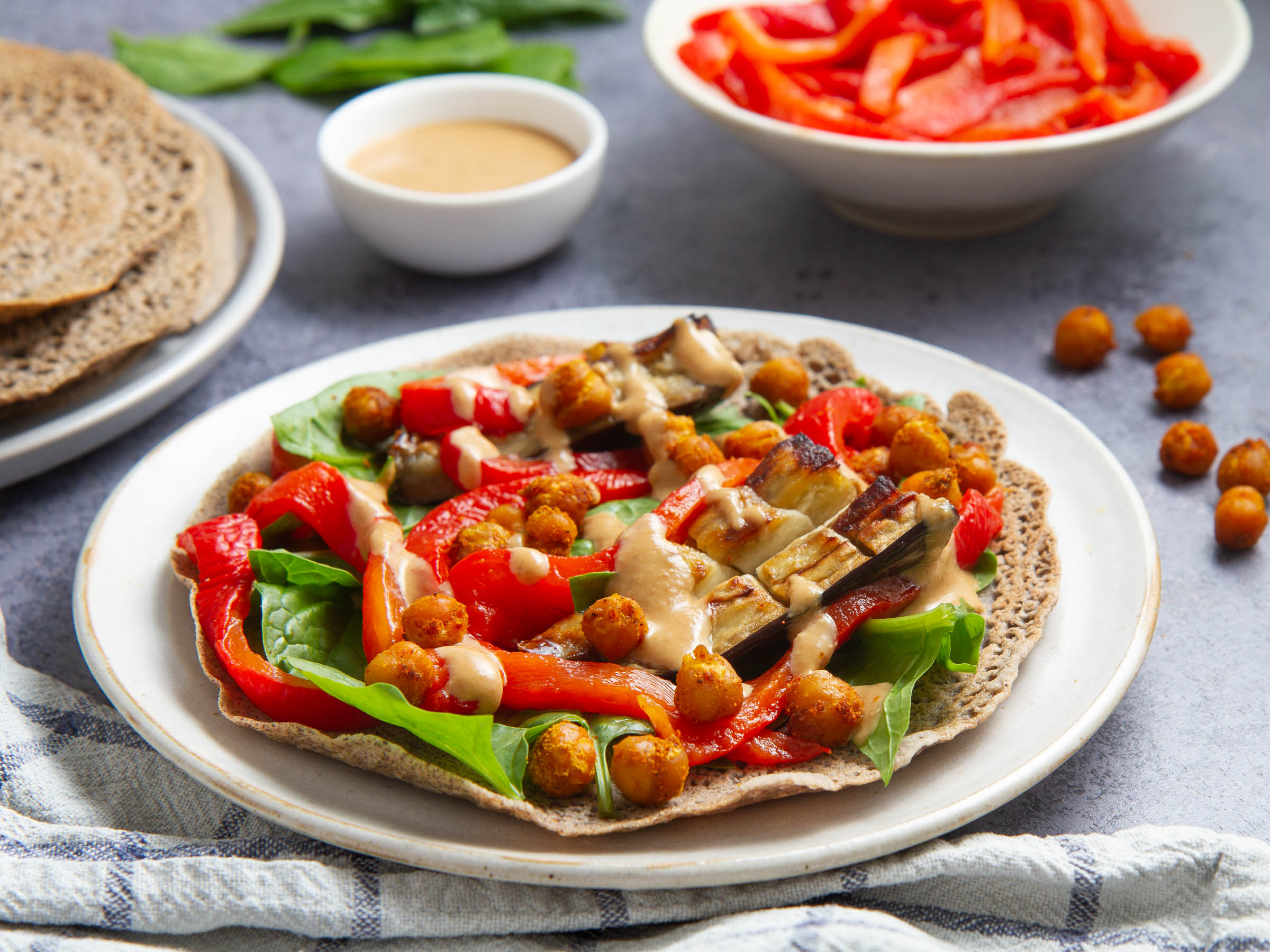 Galettes de sarrasin garnies aux pois chiches et aubergines rôtis, poivronnade, pousses d'épinards et sauce tahin-miso (vegan, sans gluten)