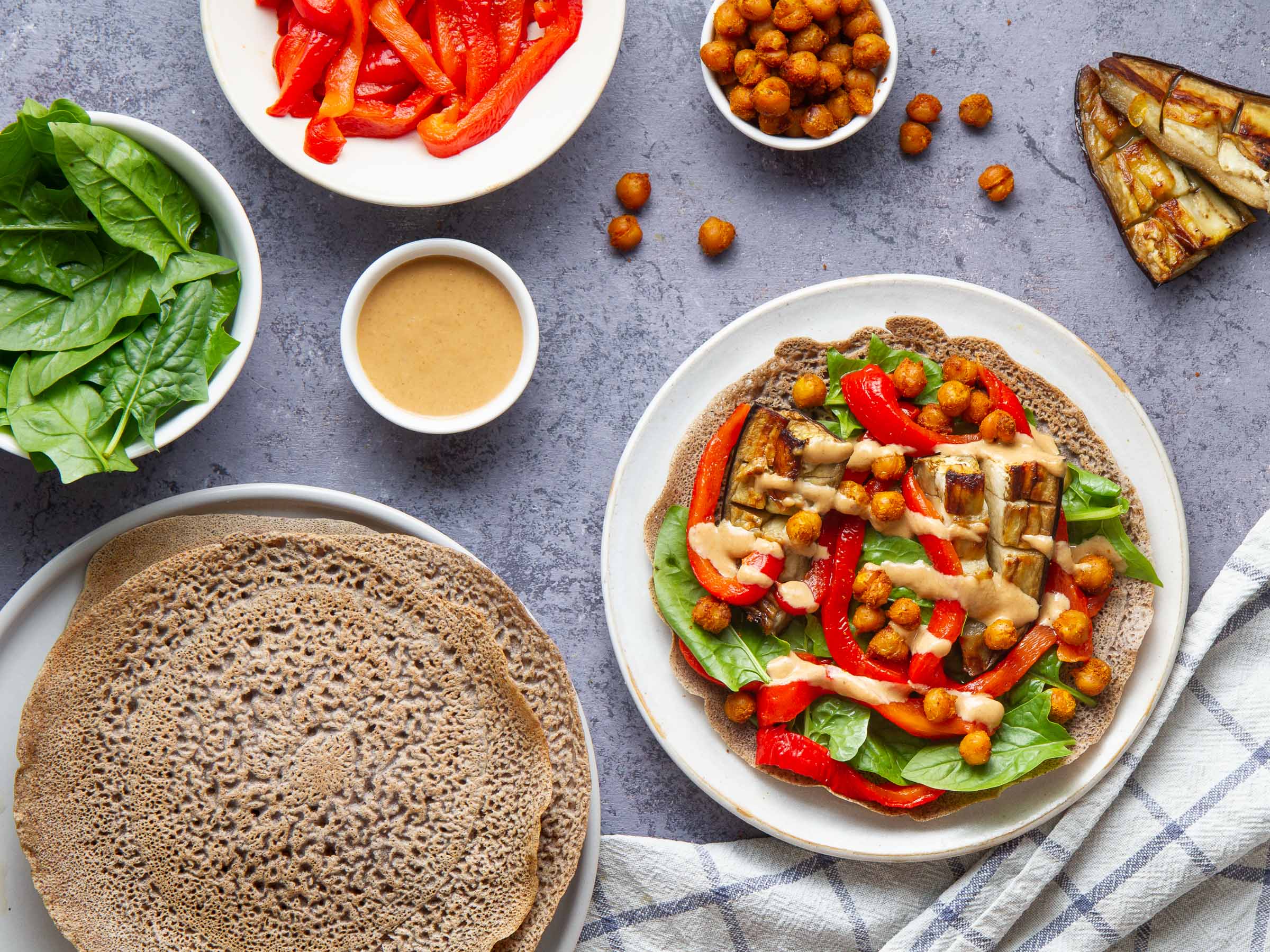 Galettes de sarrasin garnies aux pois chiches et aubergines rôtis, poivronnade, pousses d'épinards et sauce tahin-miso (vegan, sans gluten)